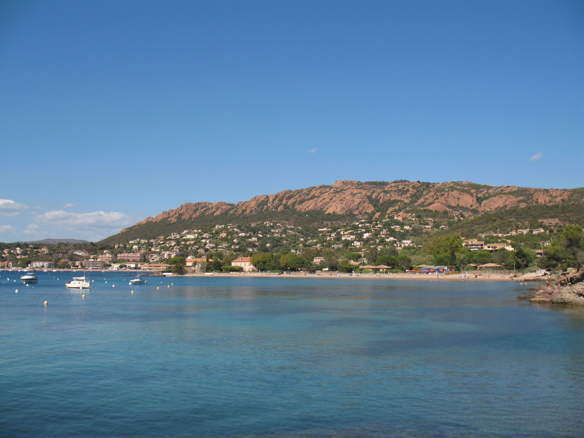 A coastal town with a mountain in the background, calm water, and boats.