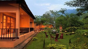 A hotel with a covered outdoor area, a well-maintained garden with various plants and trees, and a view of the surrounding landscape. - KAZIRANGA ECO VILLAGE RESORT (Kaliabar)