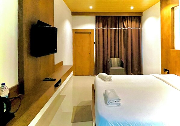 Habitación de hotel con una cama, un televisor montado en la pared, una silla y una puerta.