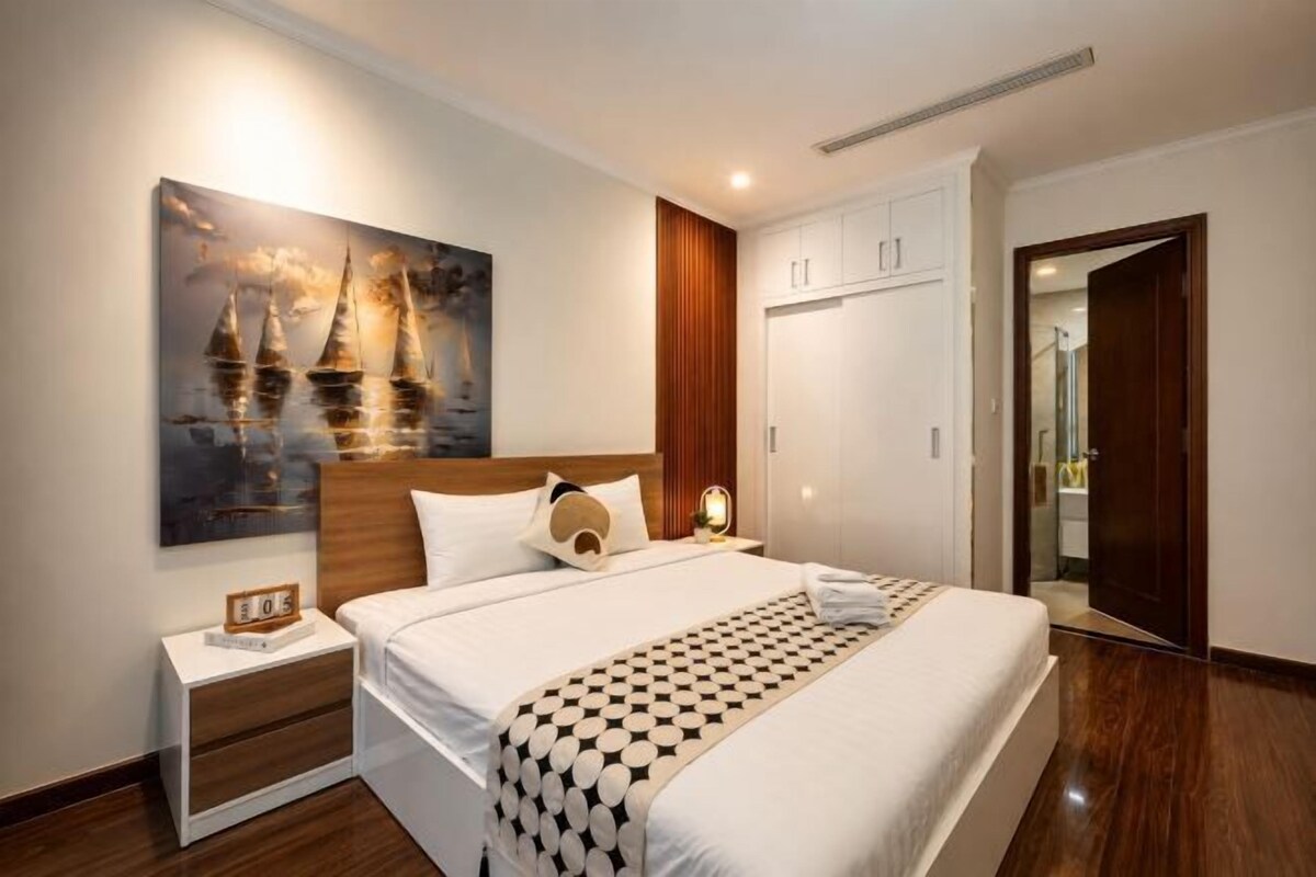A hotel room with a large bed, a nightstand, a wall-mounted painting, and a wooden door.