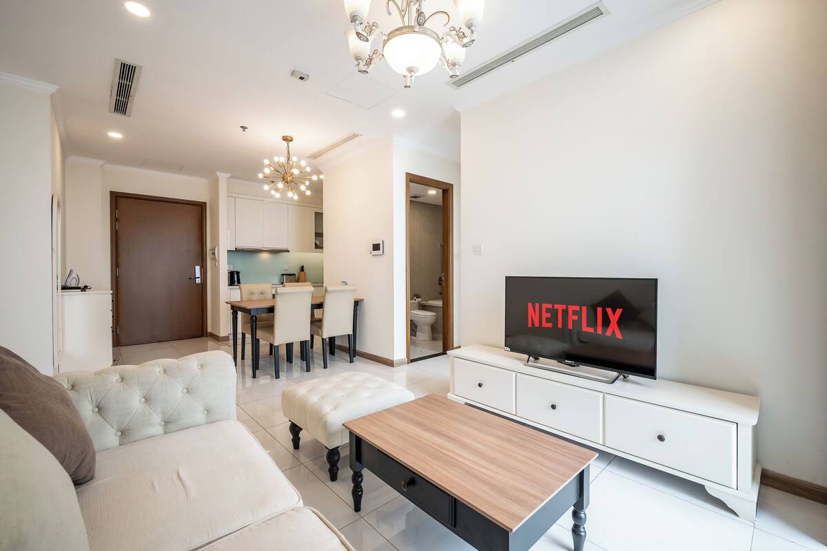 A modern living room with a TV displaying the Netflix logo, a sofa, a coffee table, and a dining area in the background.