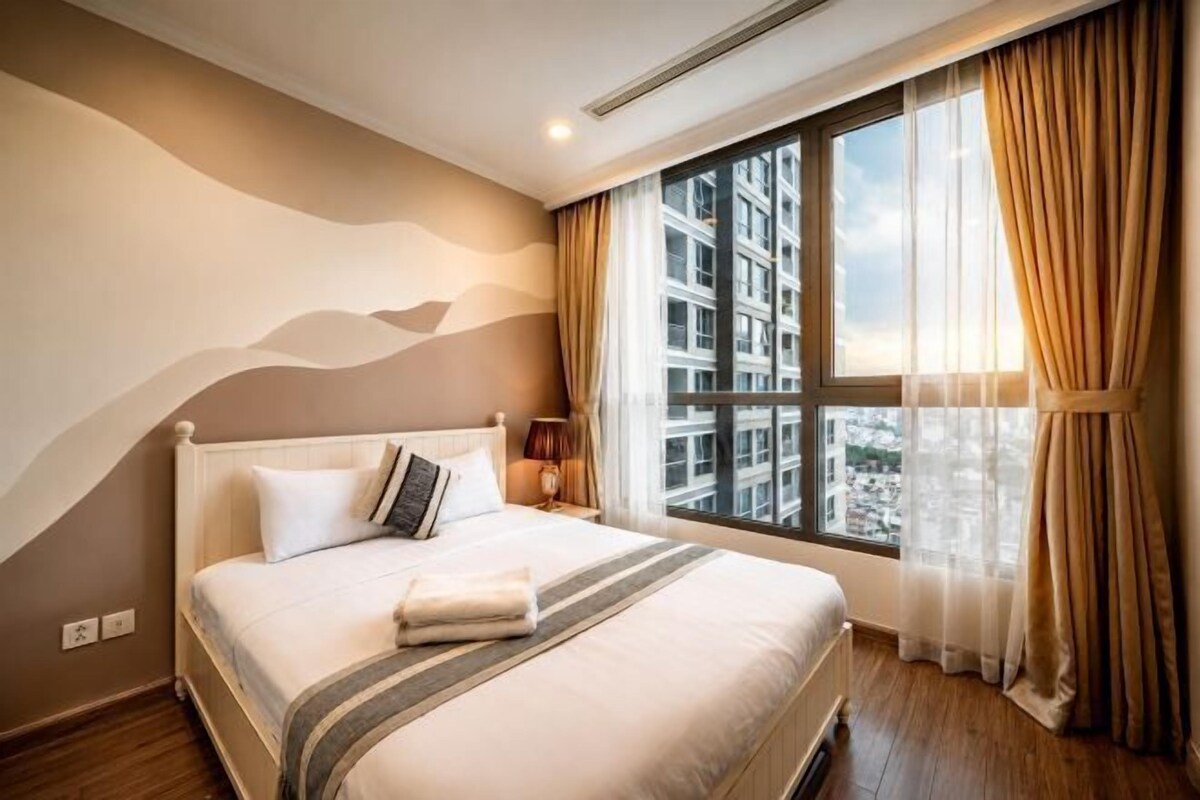 A hotel room with a large bed, a view of a cityscape through a window, and a modern design.