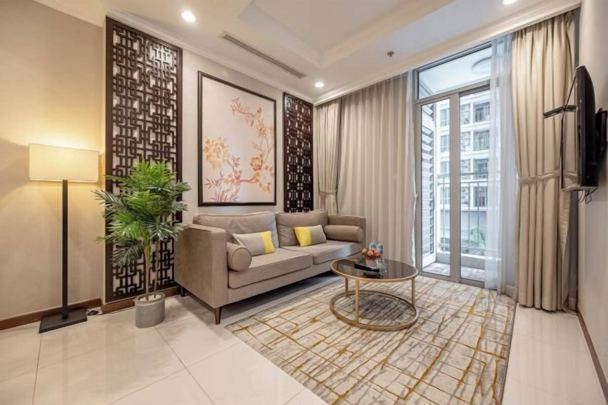 A modern living room with a sofa, a coffee table, a potted plant, and a large window with curtains.