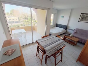 A room with a bed, a sofa, a table, and a chair. There is a balcony with a table and chairs outside. - Les Rives Latines by Interhome (Fréjus)