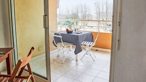 A balcony with a table and chairs, a view of trees and buildings, and a door leading to the interior. - Les Rives Latines by Interhome (Fréjus)