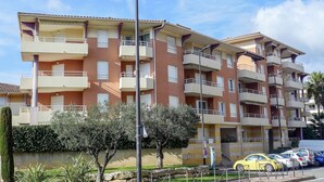 A multi-story residential building with balconies, a parking area, and a small garden area with trees. - Les Rives Latines by Interhome (Fréjus)