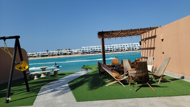 Un patio frente a la playa con un columpio, una zona de estar y vistas al océano y los edificios del hotel.