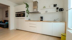A modern kitchen with white cabinets, a wooden countertop, and a built-in oven. There is a small plant on the wall and a yellow trash bin. - Sea of Tranquility with terrace by Interhome (Oostende)