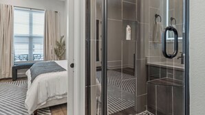 A modern hotel room with a bed, a shower area with a glass door, and a view of the outdoors through the window. - Luxury Downtown Townhouse w/ Game Room and Gated Lot (Tyler)