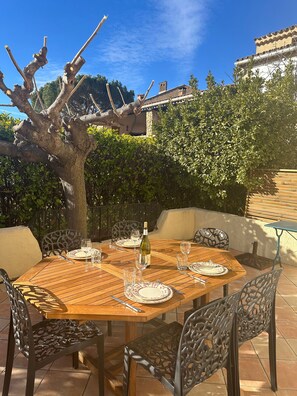 Un área de comedor al aire libre con una mesa de madera dispuesta para cuatro personas, rodeada de sillas de metal.