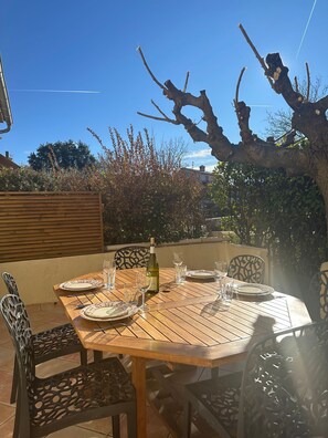 Mesa de madera preparada para comer, con sillas, una botella de vino y copas.