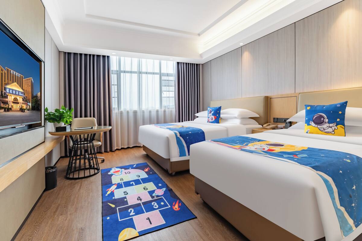 A hotel room with two beds, a desk, a TV, and a window with curtains.