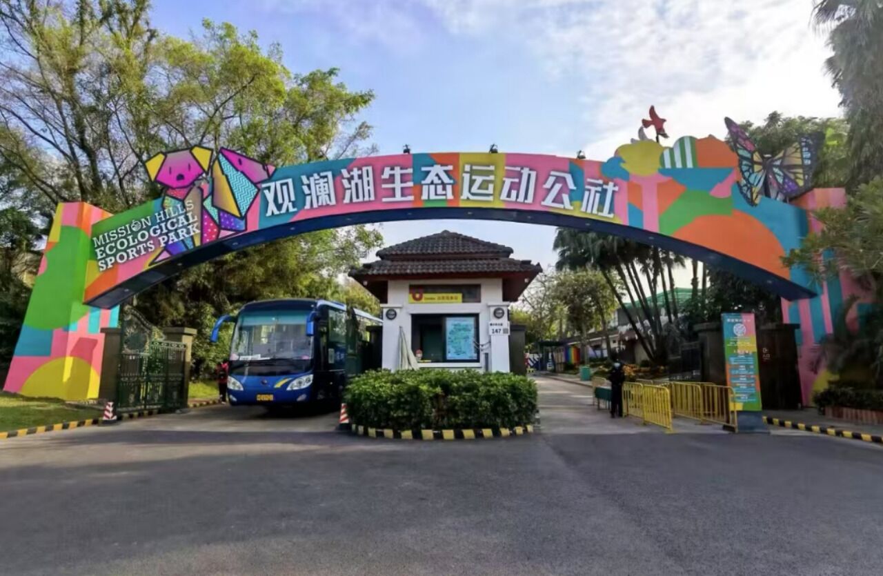 A colorful archway with text and logos, a bus, and a small building with a sign.