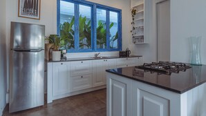 Una cocina moderna con armarios blancos, un refrigerador de acero inoxidable, un ventanal con marco azul y una estufa a gas.