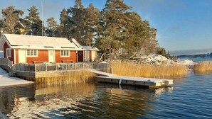 A wooden dock extending into a calm lake, with a red building featuring a white roof and a small deck area. - Kapteenin huvilat by Interhome (Parainen)