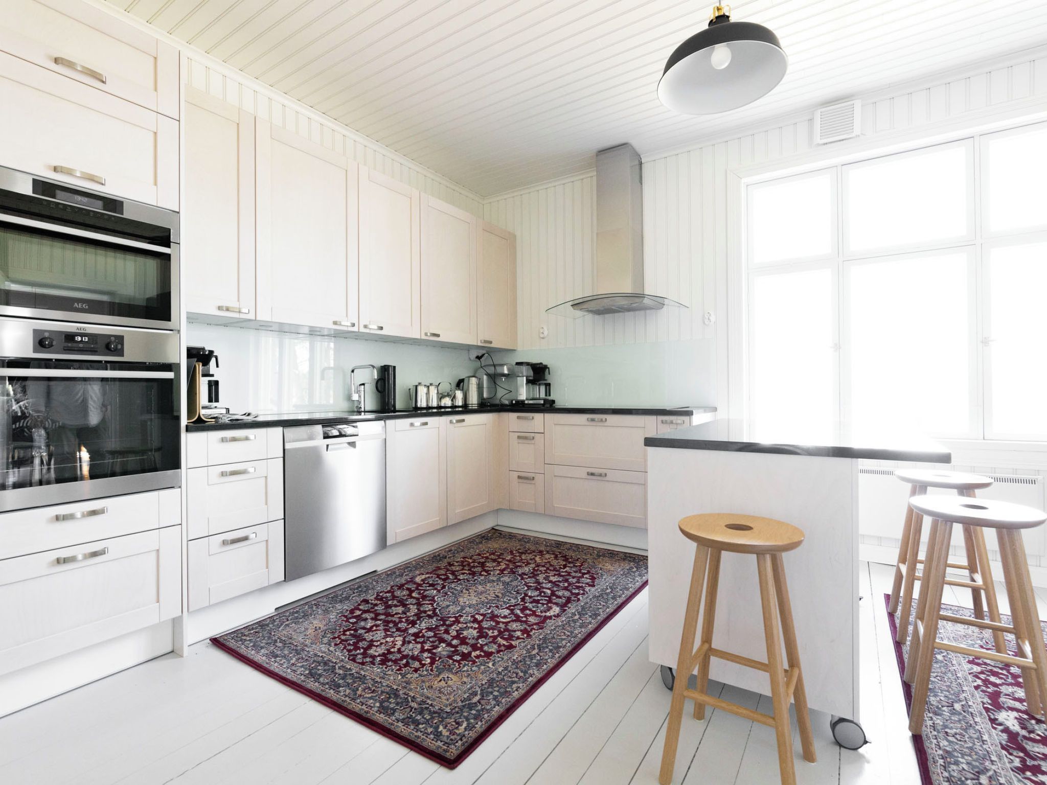 Una cocina moderna con muebles blancos, electrodomésticos de acero inoxidable, encimera negra y una alfombra estampada.