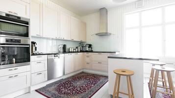 Una cocina moderna con muebles blancos, electrodomésticos de acero inoxidable, encimera negra y una alfombra estampada.