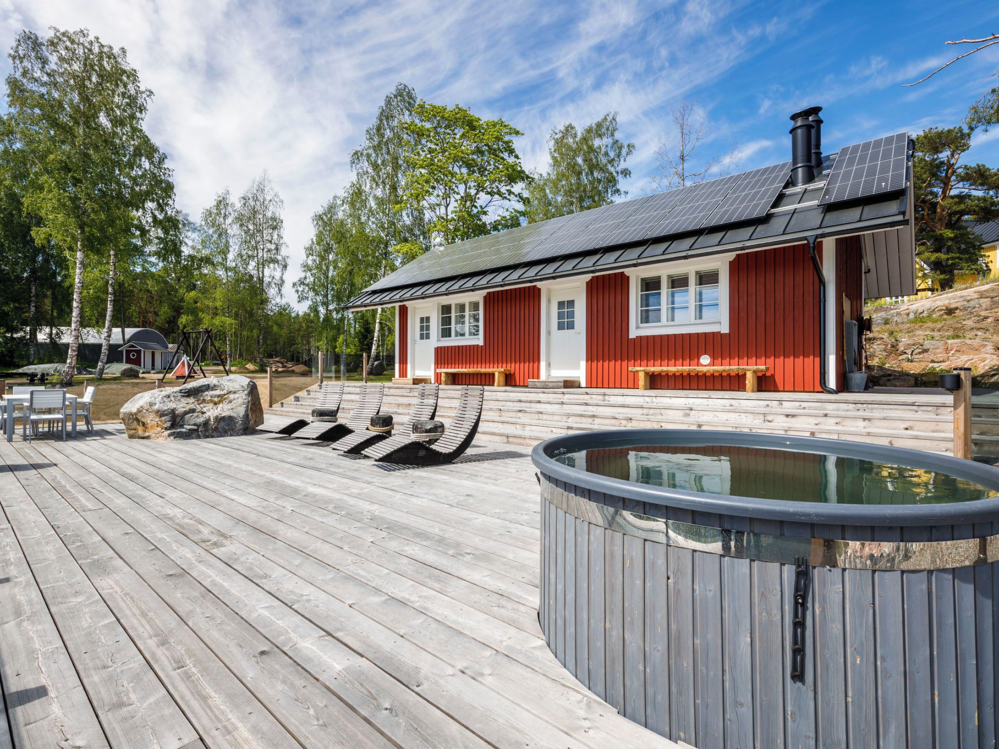 A wooden deck with lounge chairs, a hot tub, and a red building with windows.