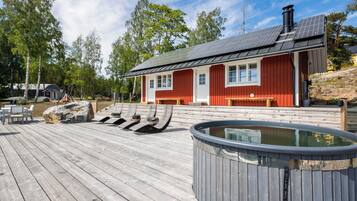 A wooden deck with lounge chairs, a hot tub, and a red building with windows.