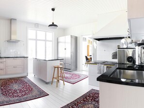 A modern kitchen with white cabinetry, a stainless steel refrigerator, a black countertop, and a red patterned rug.
