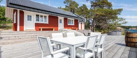 A wooden deck with a white table and chairs, a red building with windows, and a clear sky.