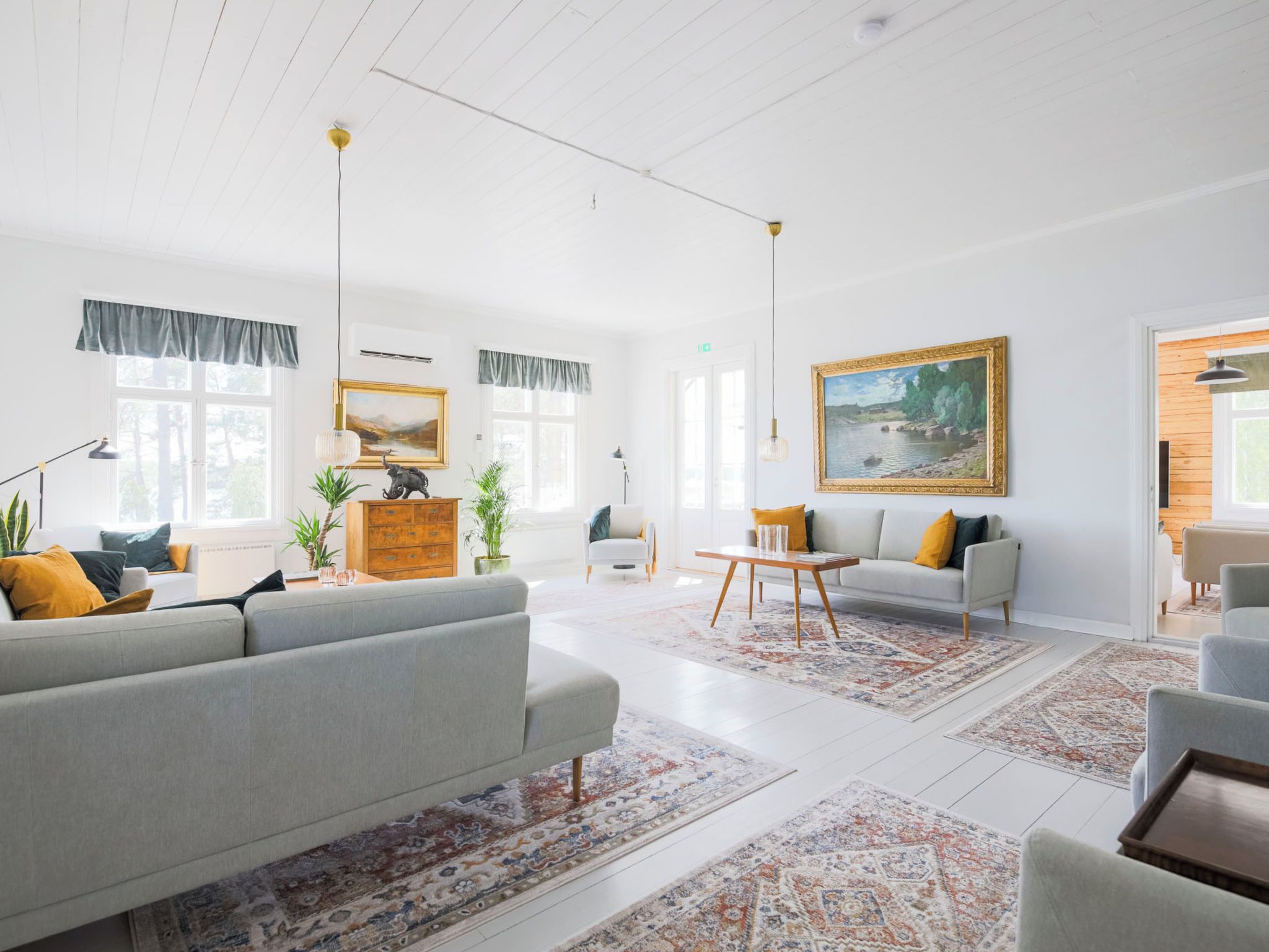A spacious living room with a grey sofa, a white armchair, a wooden coffee table, and a painting on the wall.