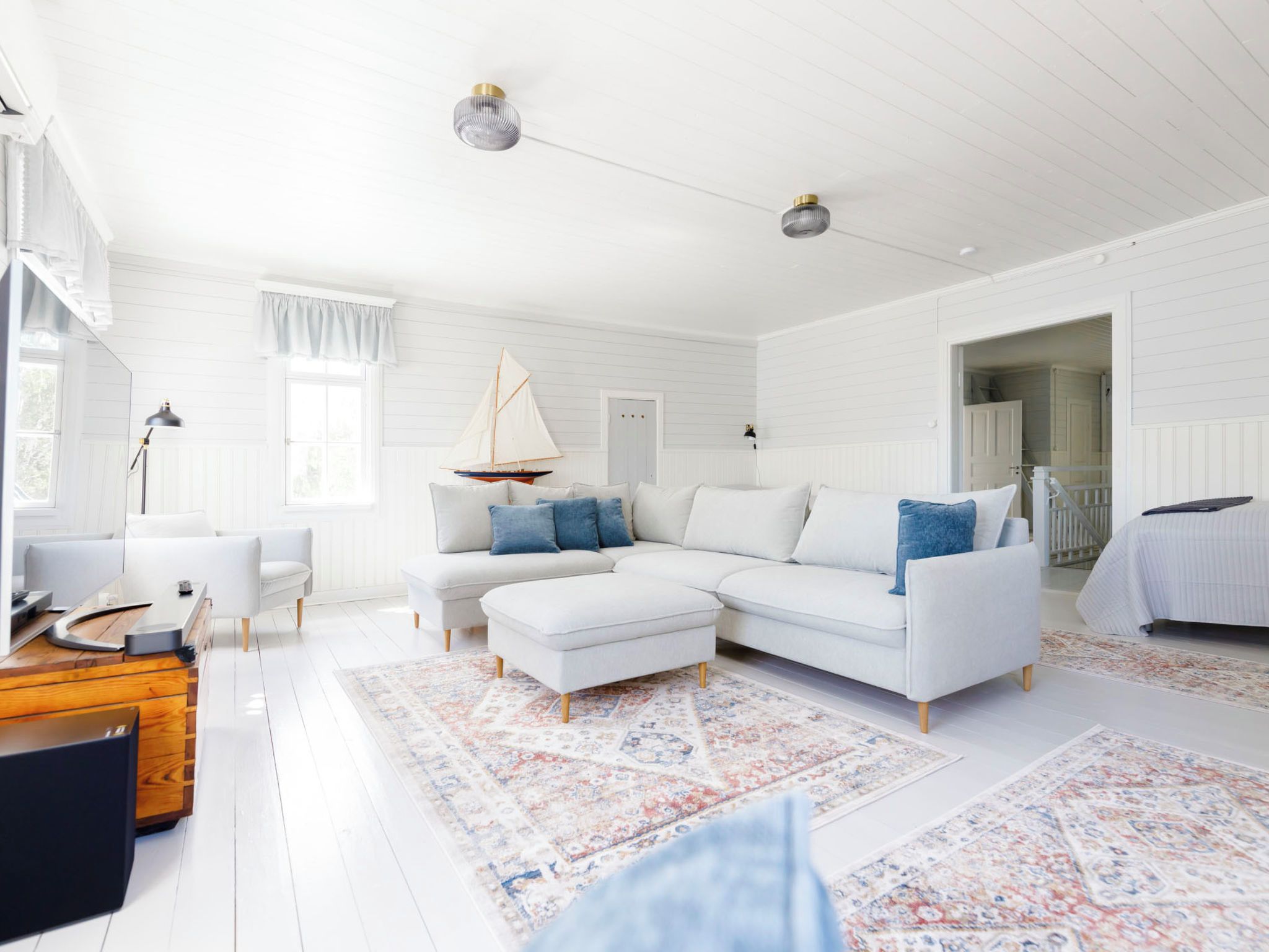 Amplia sala de estar con un sofá blanco, reposapiés y una decoración náutica.