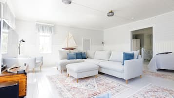 Amplia sala de estar con un sofá blanco, reposapiés y una decoración náutica.