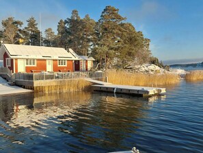 En hytte med en anløbsbro, der strækker sig ud i en rolig sø, omgivet af træer og en klar himmel.