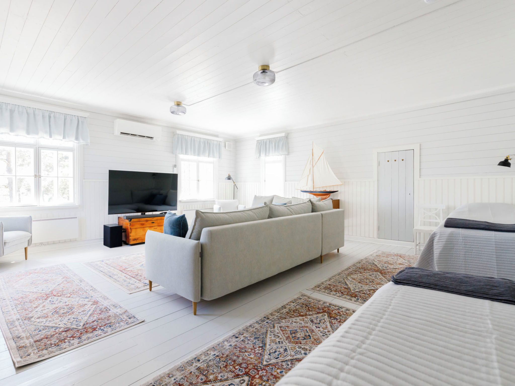A spacious room with a large sofa, a television, a sailboat decoration, and a bed.
