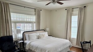 A bedroom with a bed, a chair, a nightstand, a ceiling fan, and a window with curtains.