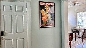 A hallway with a white door, a framed poster on the wall, and a ceiling fan.