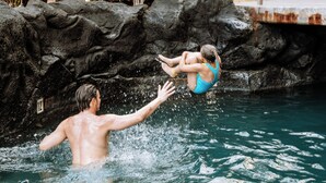 Una persona si tuffa in una piscina con una parete rocciosa sullo sfondo.
