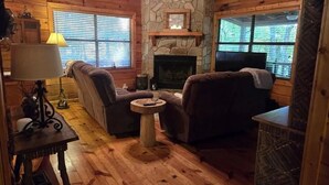 A cozy cabin interior with a stone fireplace, wooden walls, and a comfortable seating area. - Experience Serenity at Triple Nickel Cabin! (Blue Ridge)