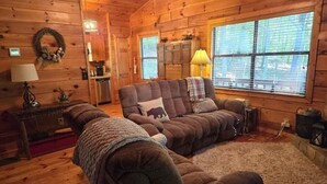 A cozy log cabin interior with a large sofa, a fireplace, and a kitchen area. - Experience Serenity at Triple Nickel Cabin! (Blue Ridge)