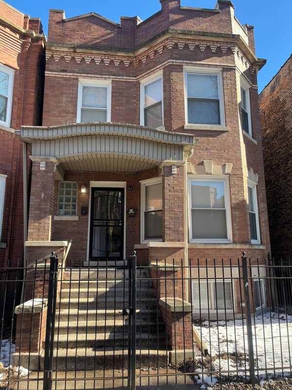 A corner brick building with a bay window, a front door, and a small porch.