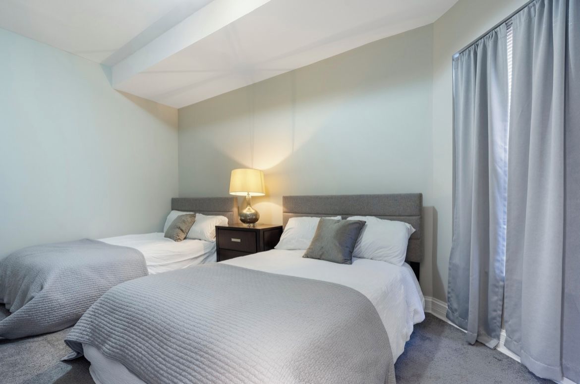A hotel room with two beds, a nightstand with a lamp, and a window with curtains.
