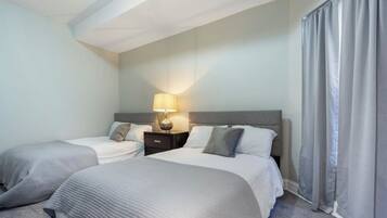 A hotel room with two beds, a nightstand with a lamp, and a window with curtains.