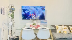 A dining area with a glass table set for two, a TV mounted on the wall, and a couch with patterned cushions. - MARIA CONDO 19F Cebu High-Rise (Mandaue City)