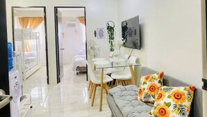 A living room with a sofa, a dining table with chairs, a TV mounted on the wall, and a ceiling light. - MARIA CONDO 19F Cebu High-Rise (Mandaue City)