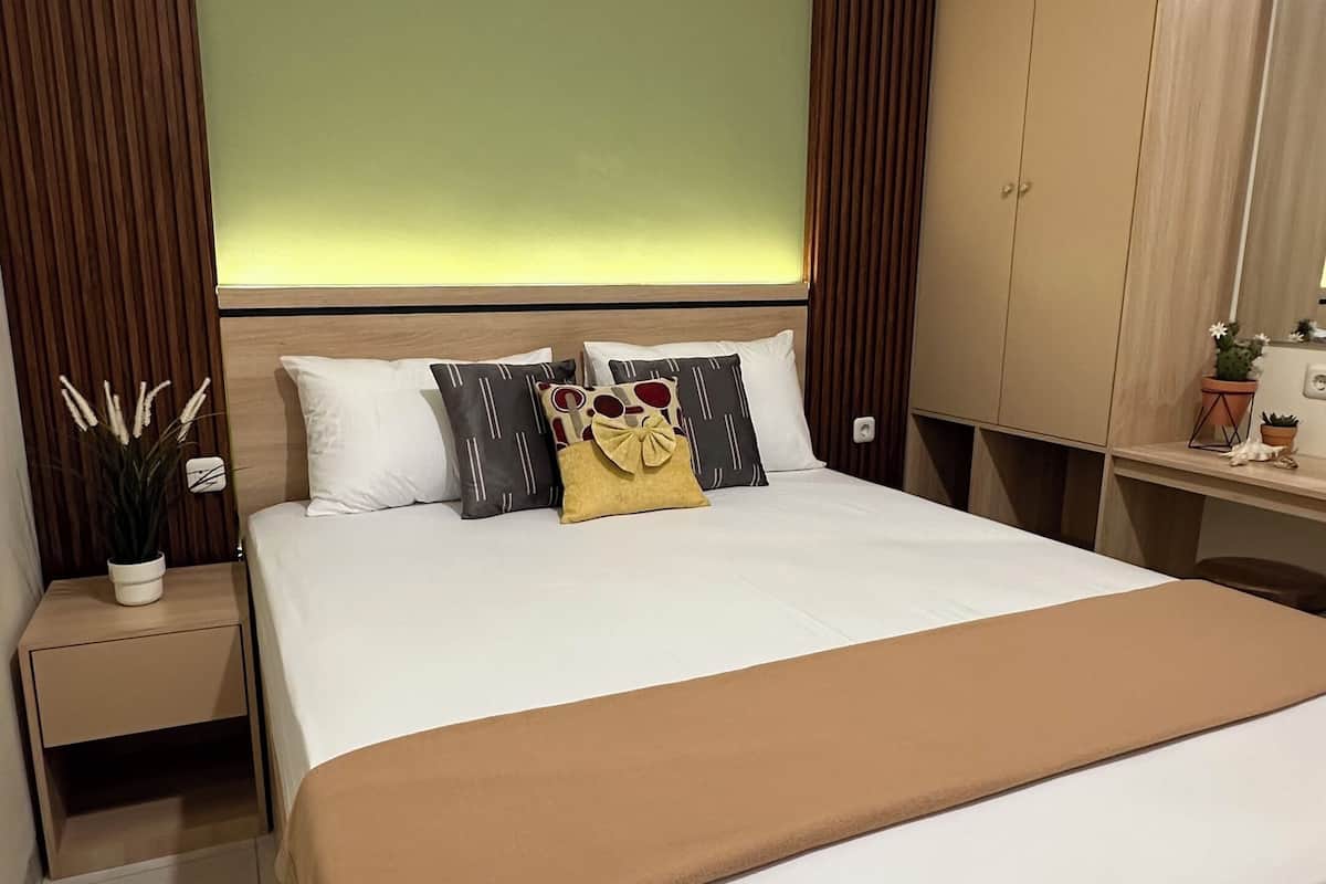 Quarto de hotel com uma cama grande, uma mesa de cabeceira, um guarda-roupa e uma pequena mesa com uma planta.