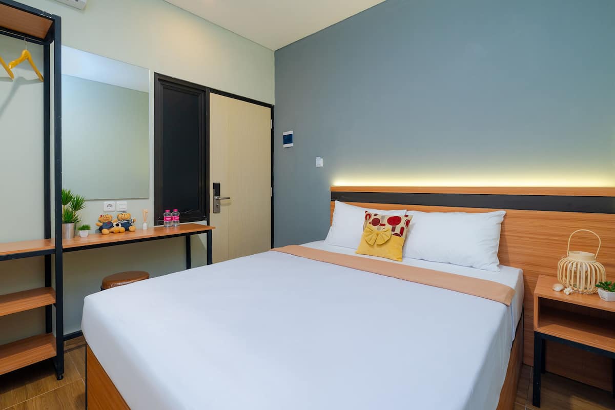Quarto de hotel com cama, escrivaninha, cadeira, guarda-roupa e mesa de cabeceira com abajur.