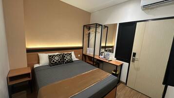 A hotel room with a bed, bedside table, a desk with a chair, a wardrobe, and a mirror.
