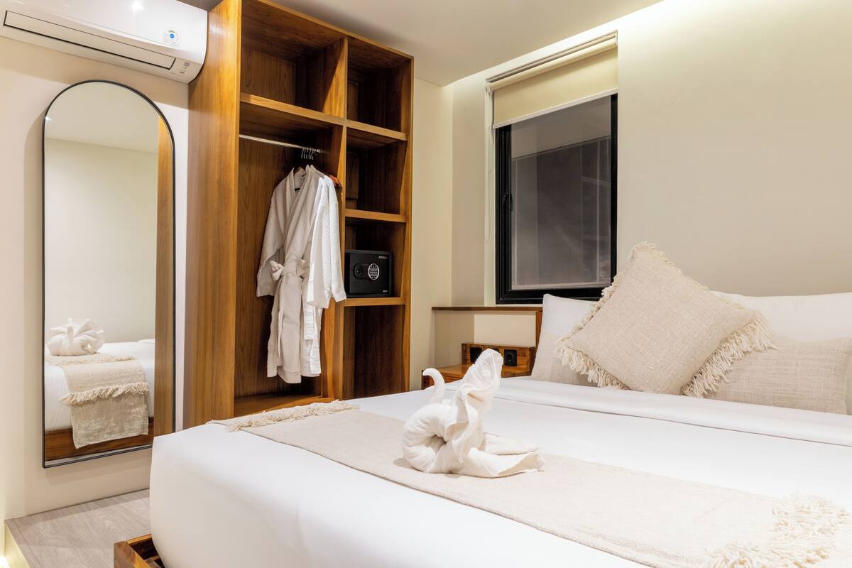 Habitación de hotel con una cama grande, un armario de madera, un espejo, un televisor y una escultura de toalla sobre la cama.