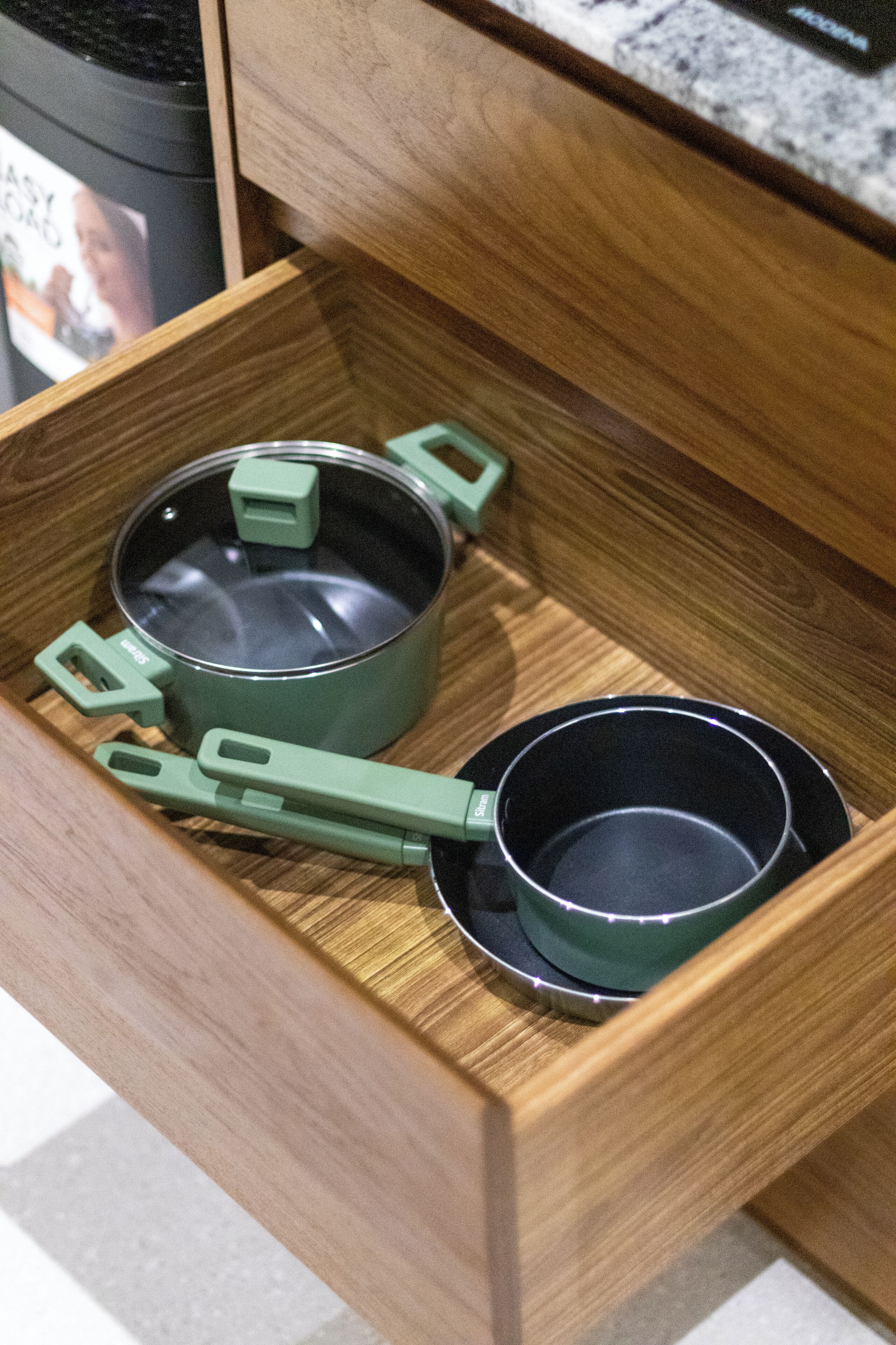 A wooden drawer containing two green pots and a matching lid.