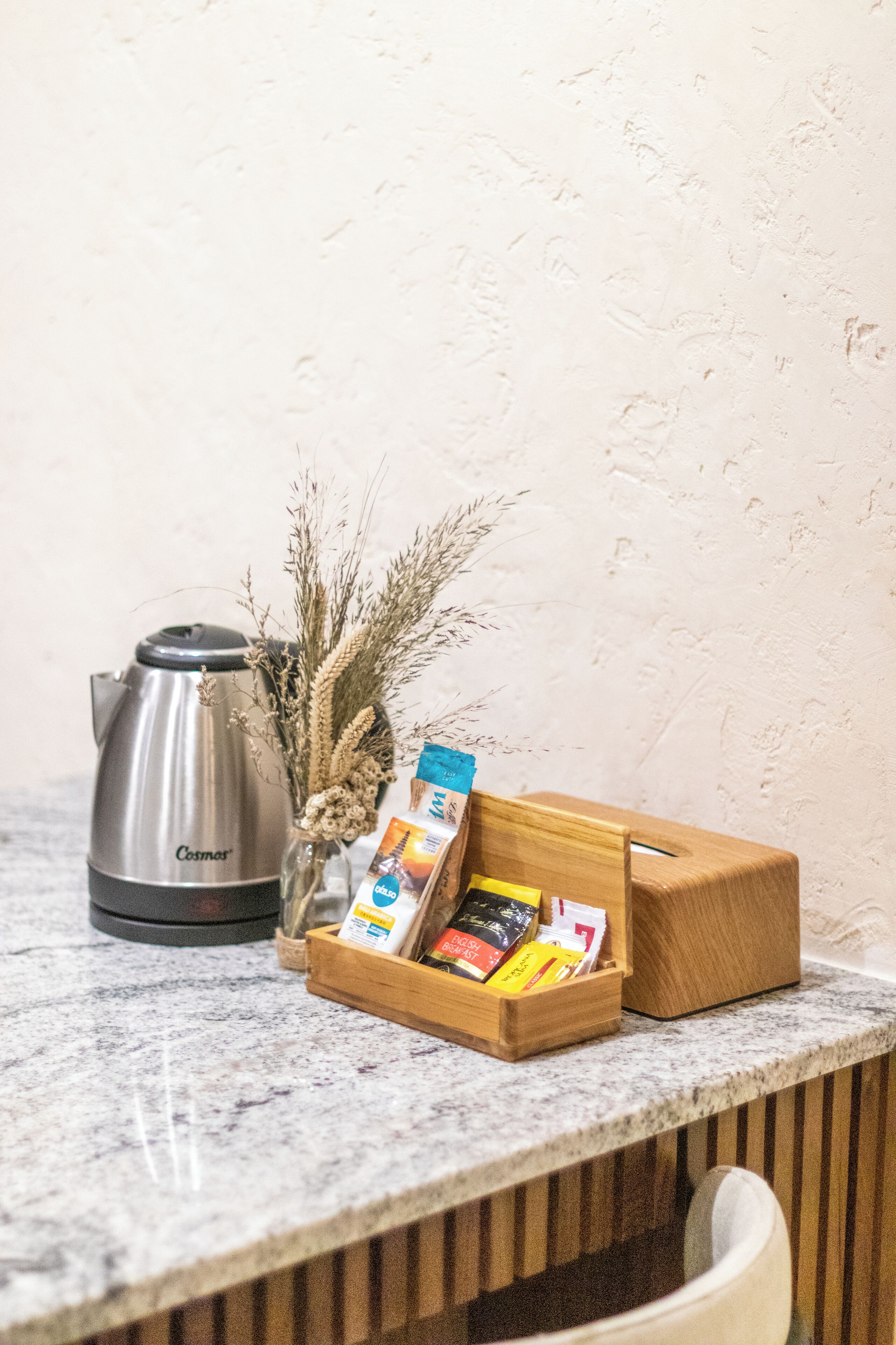 A kitchen counter with a coffee maker, a wooden box with snacks, and dried plants.