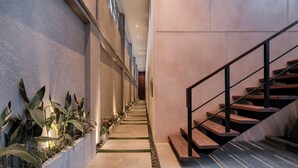 Un interior moderno con una escalera, paredes de concreto y plantas en macetas a lo largo del pasillo.