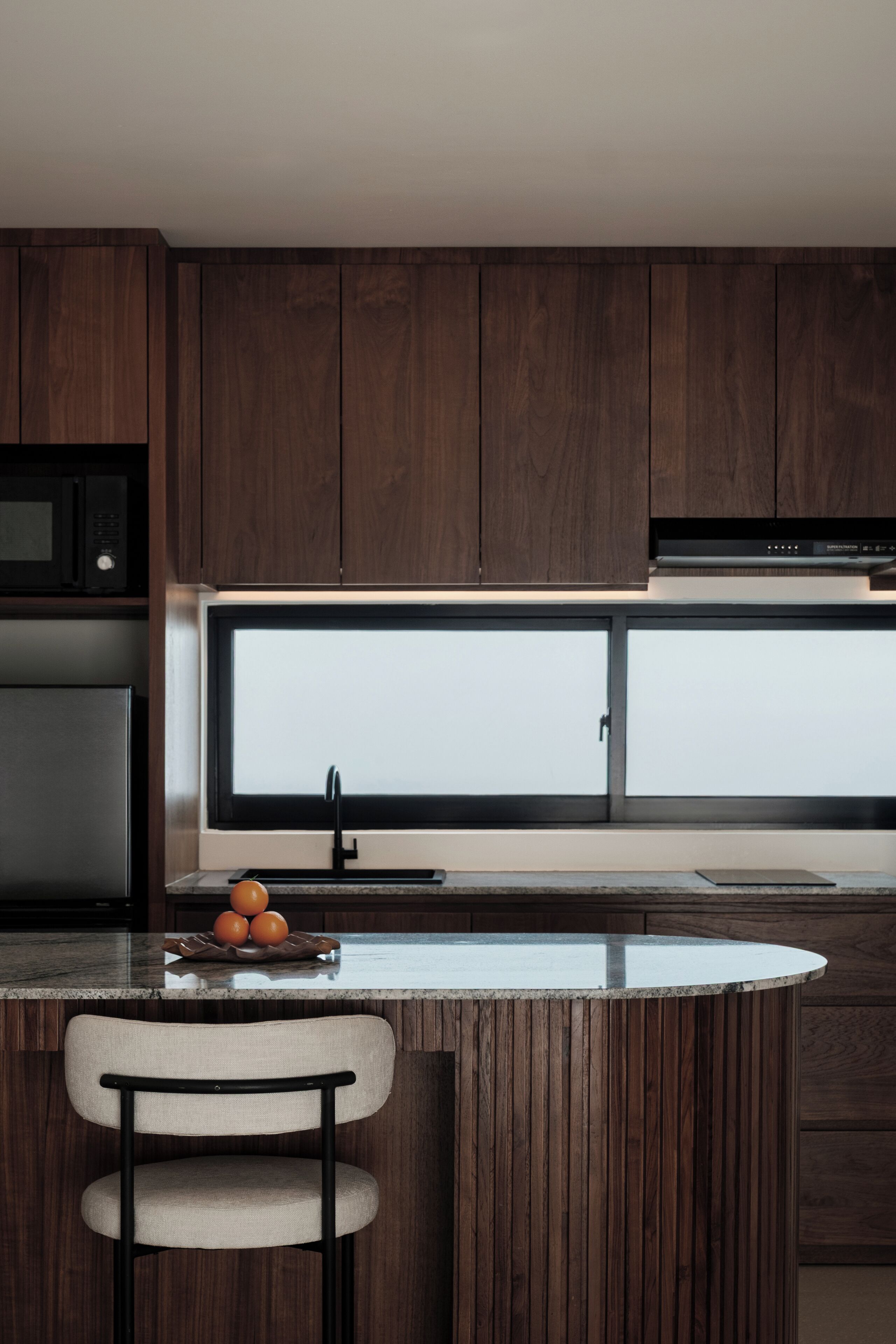 A modern kitchen with dark wood cabinets, a stainless steel refrigerator, a microwave, and a large window above the sink.