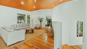 Amplia sala de estar con techo de madera, un conjunto de sofás, una mesa de centro y un gran ventanal con vistas a la vegetación.