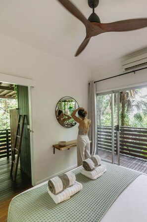 Un dormitorio con cama, espejo, ventilador de techo y vistas al exterior.